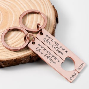 May include: Rose gold keychain set with two tags. The tags are engraved with the text "Where it all began" and coordinates. The date "07.18.24" is engraved on both tags.