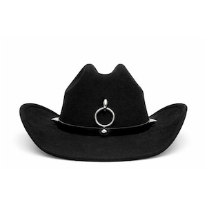Puede incluir: Un sombrero de vaquero negro con un anillo y tachuelas plateadas. El sombrero tiene un ala curvada y un anillo decorativo plateado en la parte delantera. El sombrero es de fieltro.