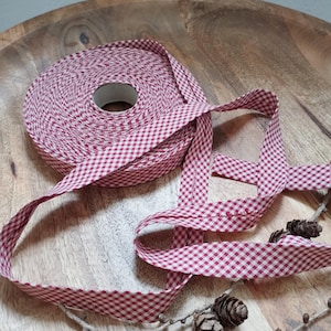 Könnte beinhalten: Eine Rolle rotes und weißes Gingham-Band mit weißem Mittelteil. Das Band liegt auf einer Holzoberfläche mit Tannenzapfen.