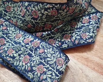 Puede incluir: Cinta floral azul marino con un patrón repetido de flores rosas y hojas verdes. La cinta está doblada y colocada sobre una superficie de madera. Los bordes de la cinta son de un azul marino más oscuro.