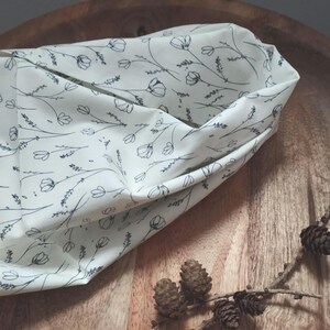 Könnte beinhalten: Cremefarbener Stoff mit schwarzem Blumenmuster, gefaltet, um die Innenseite zu zeigen. Der Hintergrund zeigt eine Holzschale und einen Kiefernzweig. Ideal für Bastelarbeiten.