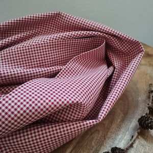 Könnte beinhalten: Rotes und weißes Gingham-Gewebe mit einem kleinen karierten Muster. Der Stoff ist gefaltet und auf einer Holzoberfläche drapiert.