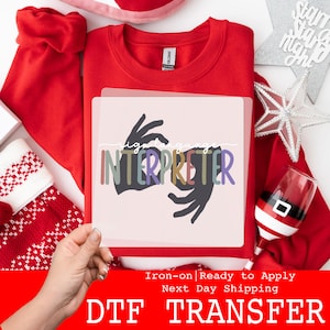 May include: A red crewneck sweatshirt with a sign language interpreter design. The design features the word "INTERPRETER" in various colors, with hands forming the sign language symbol. The image also includes the text "Iron-on | Ready to Apply" and "DTF TRANSFER".