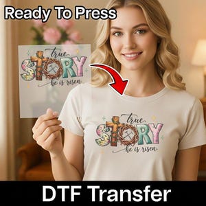 May include: A beige t-shirt featuring the words "True Story" and "he is risen". The design incorporates a cross, a crown of thorns, and floral patterns. The phrases "Ready To Press" and "DTF Transfer" are also displayed.