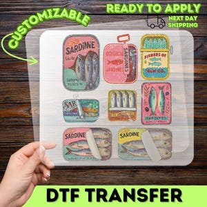 May include: A DTF transfer sheet featuring various vintage sardine can designs. The cans are in different shapes and colors, with text like "Sardine" and "Original". The sheet also includes the text "Ready to Apply" and "Next Day Shipping".