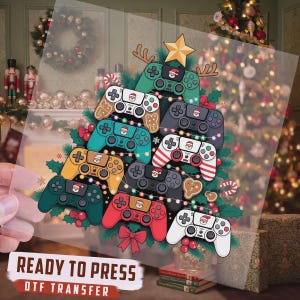 May include: A DTF transfer sheet featuring a Christmas tree design composed of various colorful video game controllers, decorated with a gold star, string lights, and gingerbread cookies, with the text READY TO PRESS DTF TRANSFER.
