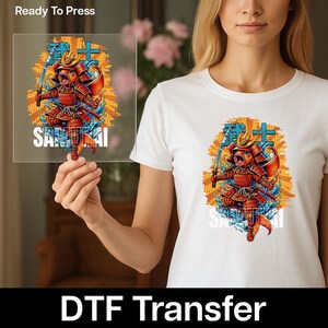 May include: White t-shirt with a vibrant graphic of a samurai fish holding a sword. The design incorporates Japanese characters and the word "SAMURAI". The image is held up to show the design on a DTF transfer.