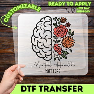 May include: A clear DTF transfer sheet featuring a graphic design of a human brain on the left side and a collection of red and orange flowers with green leaves on the right side. Below the graphic, the text reads Mental Health MATTERS.