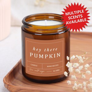 Może przedstawiać: Brązowy szklany słoik na świecę z białym knotem i etykietą z napisem "hey there PUMPKIN". Na etykiecie widnieje również napis "Sea salt sage" i "42 HRS". Czerwony wykres mówi "MULTIPLE SCENTS AVAILABLE".