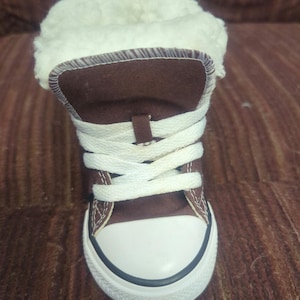 Könnte beinhalten: Braune Canvas-High-Top-Sneaker mit weißen Schnürsenkeln und einer weißen Gummispitze. Die Sneaker haben ein Kunstfellfutter.