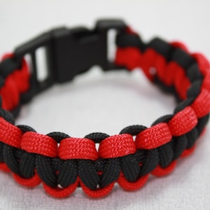 May include: A black and red paracord bracelet with a black plastic buckle.