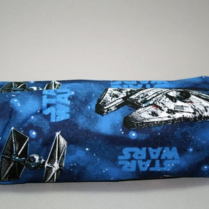 Könnte beinhalten: Eine blaue und schwarze Star Wars-Reißverschlusstasche mit Weltraumhintergrund. Die Tasche zeigt den Millennium Falcon, TIE-Jäger und das Star Wars-Logo.