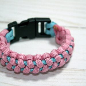 May include: A pink and blue paracord bracelet with a black plastic buckle closure.