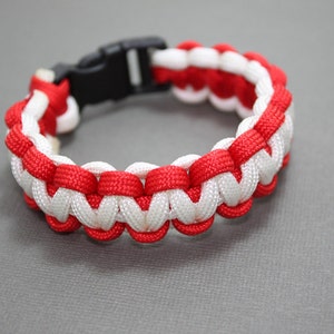 May include: A red and white paracord bracelet with a black plastic clasp.