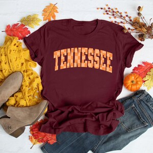 a maroon tennessee t - shirt sitting on top of a pile of fall leaves