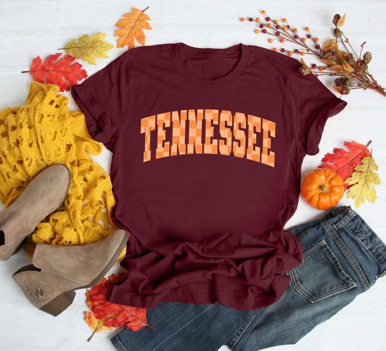 a maroon tennessee t - shirt sitting on top of a pile of fall leaves