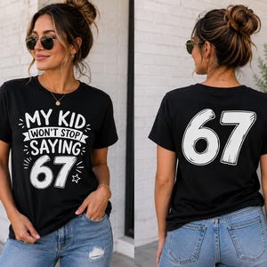 Peut inclure: Un t-shirt noir à manches courtes avec un texte graphique blanc sur le devant qui indique "MY KID WON'T STOP SAYING 67" avec des étoiles décoratives. Le dos du t-shirt affiche le grand nombre blanc "67" dans une police stylisée.