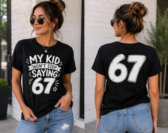 Puede incluir: Una camiseta negra de manga corta con texto gráfico blanco en la parte delantera que dice "MY KID WON'T STOP SAYING 67" con estrellas decorativas. La parte posterior de la camiseta muestra el número blanco grande "67" en una fuente estilizada.