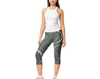 Puede incluir: Una camiseta de tirantes blanca de canalé combinada con unos leggings pirata de color verde oscuro con un patrón de líneas abstractas claras y fluidas. Los leggings llegan a media pantorrilla y el conjunto se completa con zapatillas deportivas blancas.