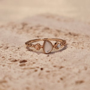 Puede incluir: Un anillo de oro con una piedra blanca y piedras más pequeñas engastadas en la banda.