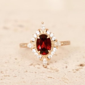 May include: A gold ring featuring a large oval red gemstone surrounded by smaller white gemstones.
