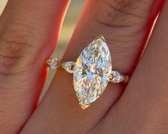 May include: A gold ring featuring a large marquise-cut center stone and two smaller pear-cut side stones. The band is thin and polished, holding the faceted clear stones in a prong setting that reflects light with a bright, brilliant sparkle.
