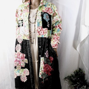 May include: A long-sleeved jacket featuring a patchwork design with a floral print upper section and a black denim lower section. The jacket includes white lace floral appliqués, embroidered red flowers, and a black pocket with a blue flower print.