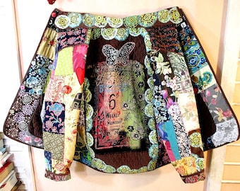 May include: A patchwork jacket featuring a brown quilted back panel with a butterfly graphic and text reading The Premier Paris, 6th, Weekly Wednesday. The garment is constructed from various floral and patterned fabric squares in shades of blue, green, pink, and yellow, with a scalloped green trim along the collar and central panel.