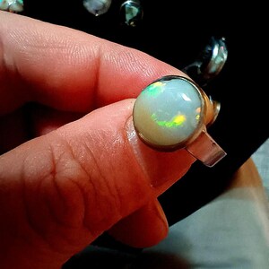 Puede incluir: Un anillo de plata con una piedra de ópalo blanco. El ópalo tiene un brillo iridiscente arcoíris.