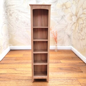 May include: A miniature wooden bookshelf with five shelves. The bookshelf is made of light brown wood and has a simple, elegant design. The top of the bookshelf has a curved arch. The bookshelf is empty and ready to be filled with miniature books and decor.