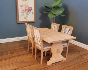 May include: A miniature wooden dining table set with four chairs. The table is made of light wood and has a simple design. The chairs are also made of light wood and have woven cane seats.