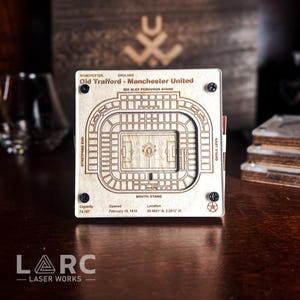 May include: A wooden laser-cut replica of Old Trafford, Manchester United's stadium, with detailed seating and field layout. The stadium's name and location are engraved, along with the capacity and opening date. The design is held together with four black screws.