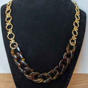 May include: A gold chain necklace with a large, brown tortoiseshell-patterned plastic chain.