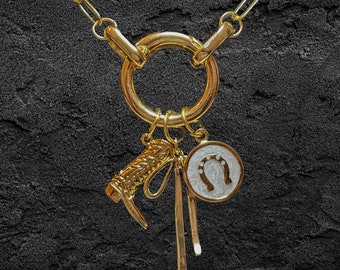 May include: A gold chain necklace with a large gold ring pendant. The pendant has several charms attached to it, including a horseshoe charm, a boot charm, and a small gold charm.