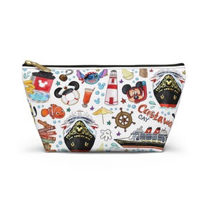 May include: White zippered cosmetic bag featuring colorful illustrations of Disney characters, cruise ships, and tropical elements. The bag includes images of Mickey Mouse, Nemo, Stitch, and a lighthouse. The words "Castaway Cay" are also visible.