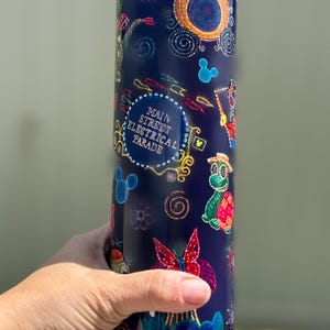 May include: A navy blue tumbler featuring a colorful design inspired by the Main Street Electrical Parade. The design includes Mickey Mouse silhouettes, a turtle, and the text "Main Street Electrical Parade".
