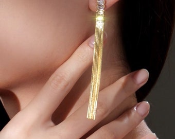 May include: Gold dangle earrings with a long, thin chain and a row of clear cubic zirconia stones at the top.