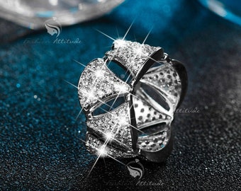 May include: A silver ring with a geometric design, featuring a large central stone surrounded by smaller stones. The ring is set against a blue background.
