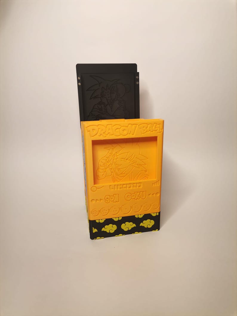 Puede incluir: Una caja de almacenamiento de color amarillo y negro con tem&aacute;tica de Dragon Ball Z con una imagen en relieve de Goku y el texto "Dragon Ball Z" y "Son Goku".