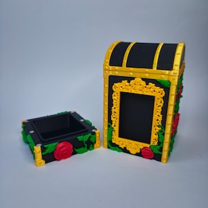 Op de afbeelding: Zwarte en gouden decoratieve kist met een bijpassende kleine doos. De kist heeft een gouden frame, rode rozen en groene wijnranken. De kleine doos is vierkant met een zwart interieur en is versierd met rozen en wijnranken.