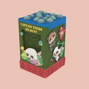 Op de afbeelding: Een decoratieve doos in groen, blauw en rood met stripfiguren en de tekst "CAPTAIN TEEMO ON DUTY". De doos heeft een schedel- en paddestoelontwerp, met een rode franje aan de onderkant en paddestoelvormige objecten erboven.