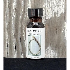 Puede incluir: Pequeña botella de vidrio marrón con aceite de perfume y tapa negra. La etiqueta dice "PERFUME OIL Sweet Grass Scent" y presenta un dibujo de hierba dulce. Contiene 14,5 ml de aceite de perfume.