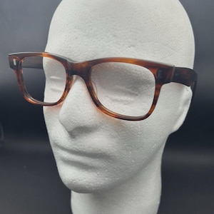 Könnte beinhalten: Braune Brille mit rechteckigem Schildpattrahmen. Die Brille wird auf einem weißen Schaumstoffkopf präsentiert. Die Fassungen haben einen klassischen, Vintage-Stil.