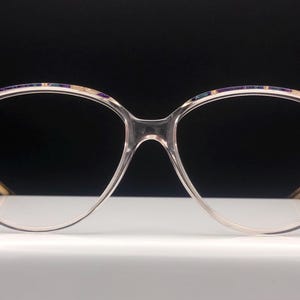 Peut inclure: Lunettes en plastique transparent avec une monture à motifs dorés et bleus. La monture a une forme œil de chat.