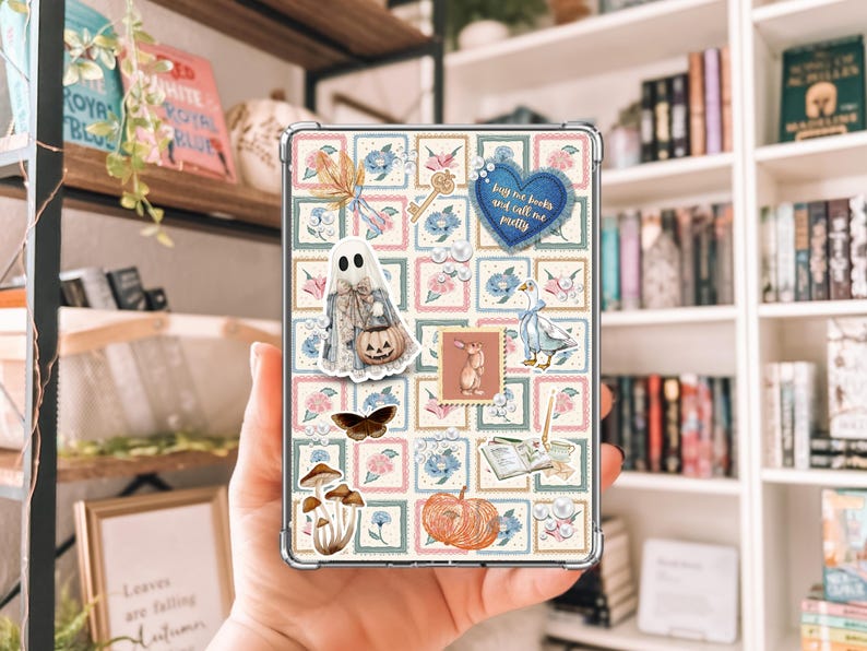 May include: A clear phone case featuring a collage of whimsical illustrations. The design includes a ghost with a pumpkin, a key, a butterfly, mushrooms, and a pumpkin. The case has a blue heart with the text "buy me books and call me pretty".