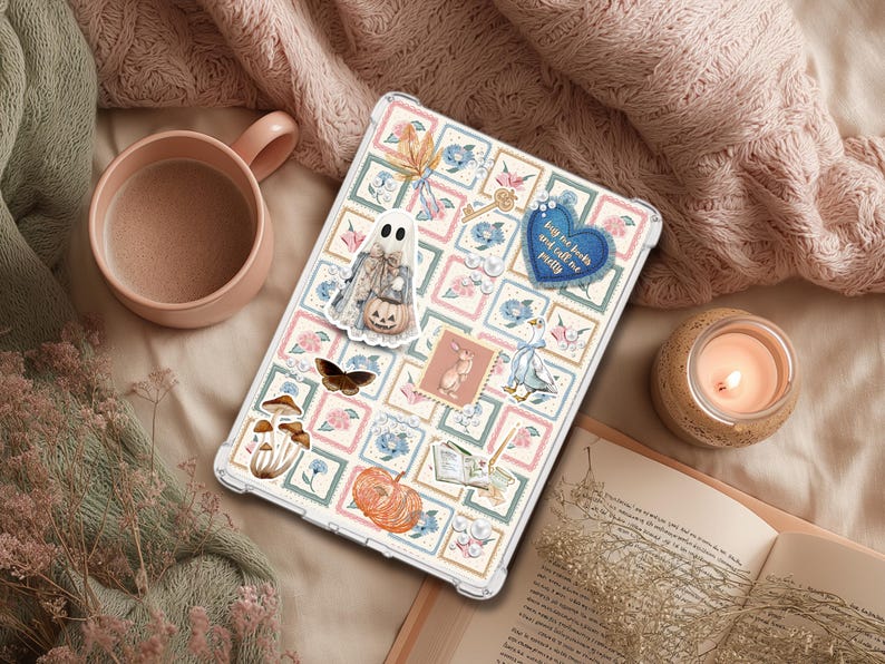 May include: A clear tablet case decorated with stickers, including a ghost, butterfly, and pumpkin. The case has a floral design with the text "buy me books and call me pretty" on a blue heart. A lit candle and a mug are also visible.