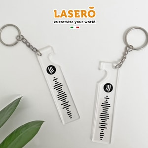 Può includere: Due portachiavi in ​​acrilico trasparente con un design a codice a barre bianco e nero e un simbolo nero a tre linee. I portachiavi sono attaccati a anelli portachiavi argentati.