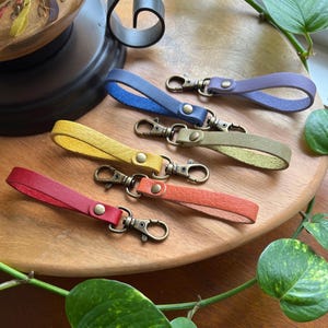 May include: Five leather keychains with different colored straps and antique gold-toned key rings. The straps are red, yellow, green, blue, and purple.