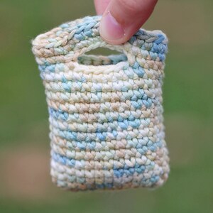 Può includere: Una piccola borsa all'uncinetto con un motivo blu e bianco. La borsa ha un manico ed è realizzata con un filato morbido e testurizzato.