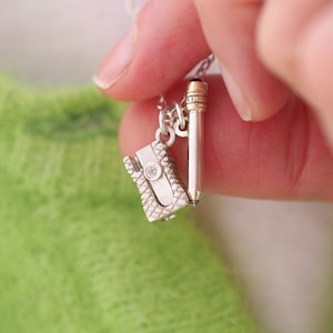 May include: A silver necklace with a pencil and a pencil sharpener charm. The pencil sharpener charm has a small diamond in the center.